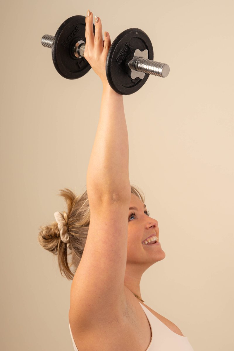 Mischa smiling while pressing a dumbbell overhead